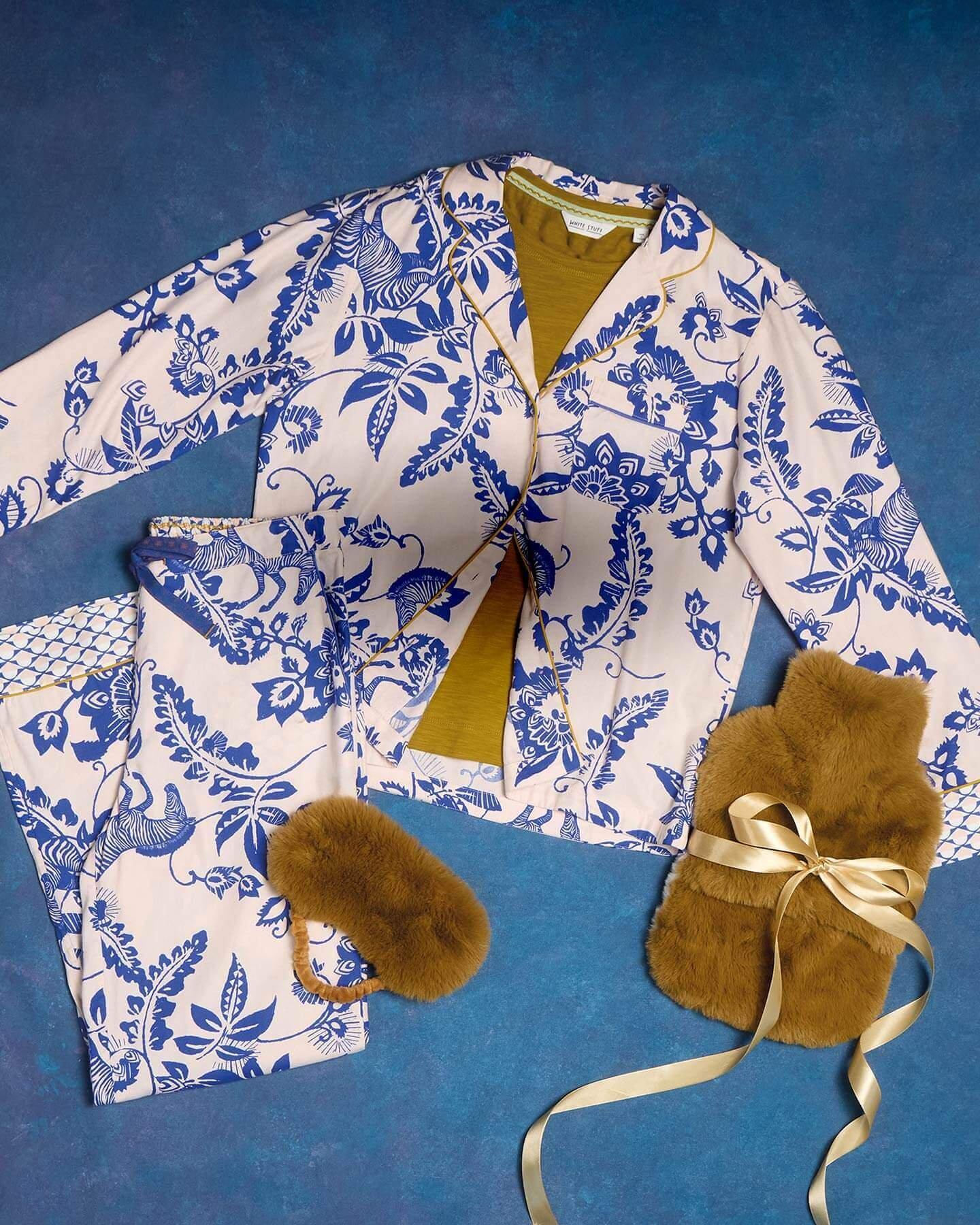 a flat lay shot of some printed women's pyjamas with a dark yellow fluffy eye mask and hot water bottle